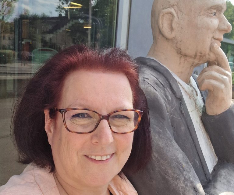 Stadtbibliothek Gersthofen Claudia Schuster posiert neben einer Skulptur eines nachdenklichen Mannes vor der Stadtbibliothek Gersthofen.